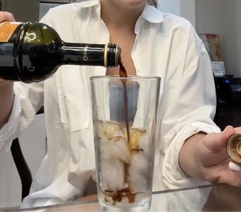 Woman in a TikTok video pouring balsamic vinegar into a glass filled with ice